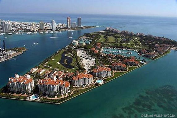 Aerial view of an island with multiple residential buildings surrounded by water and neighboring cityscape in the background.