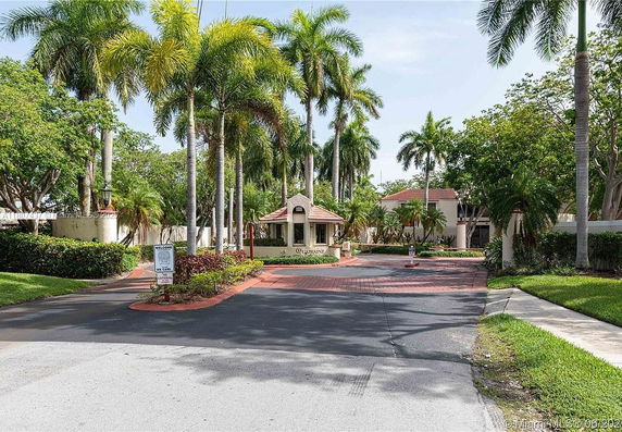 Front view of a building entrance with a guard house and palm trees.