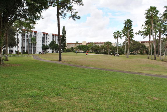 View of multi-story residential buildings with large windows and balconies, seen from a grassy area with trees.
