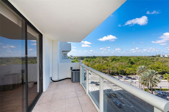 Balcony view from a building overlooking a road and lush greenery.