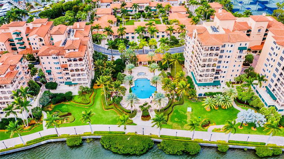 Aerial view of multi-story residential complex with a central swimming pool area and landscaped gardens, located by a waterfront.
