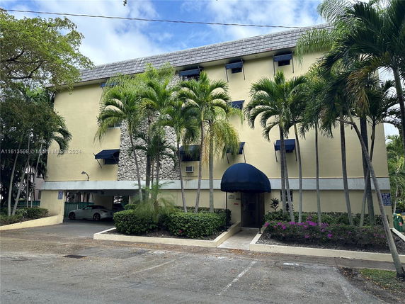 Front view of a multi-story building with palm trees and covered parking.