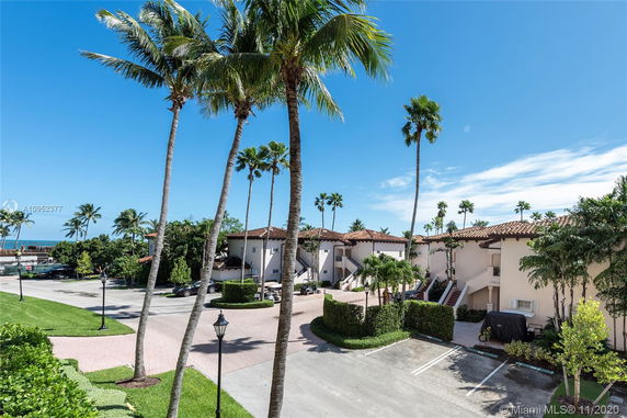 View of a group of two-story houses with red-tile roofs surrounded by palm trees.