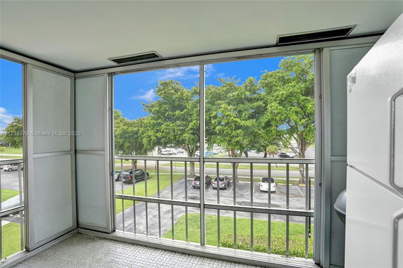 Enclosed balcony with view of trees and parked cars in a parking lot.