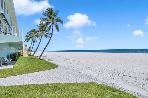 Seaside view with a partial glimpse of a building and palm trees.