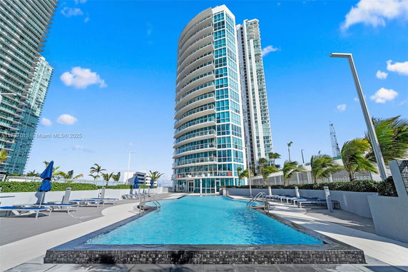 High-rise building with a curved design, featuring an outdoor swimming pool in the foreground.
