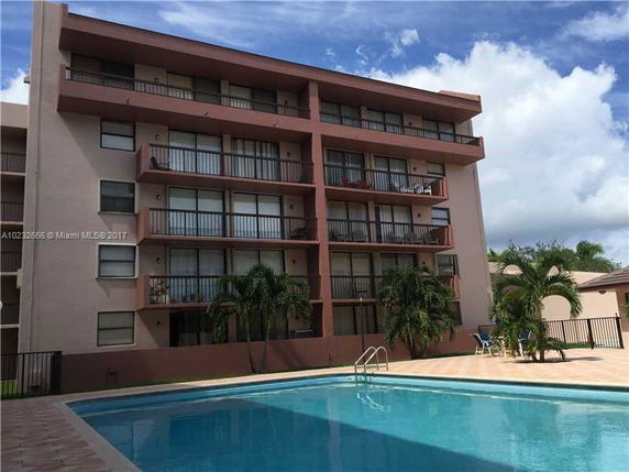 View of a multi-story residential building with balconies and a swimming pool in front.