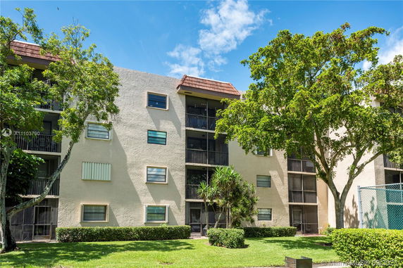 Front view of an apartment building with multiple balconies and trees in the foreground.