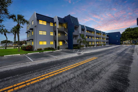 Front view of a multi-story building with illuminated windows and parking area.