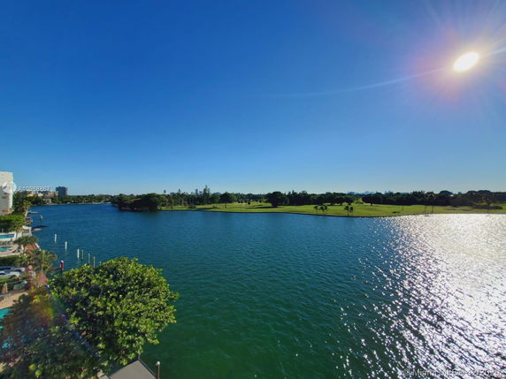 Wide-angle view over water with greenery and clear blue sky.