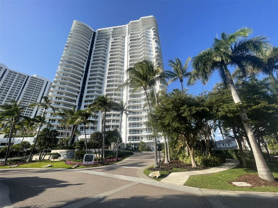 Front view of a high-rise residential building with curved balconies and palm trees.