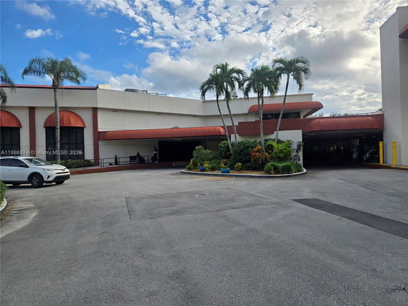 Front view of a building with red awnings and palm trees.