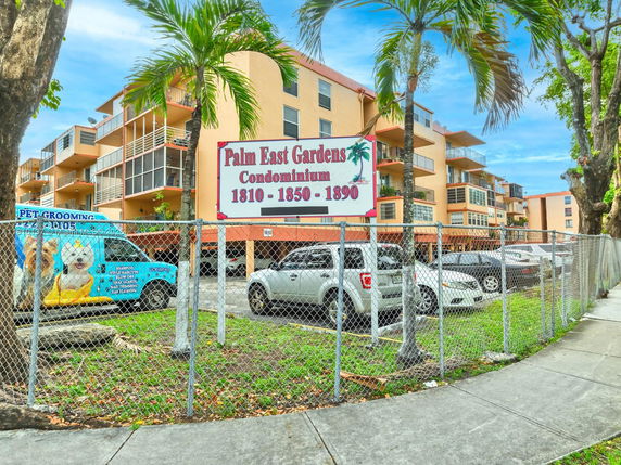 Front view of a condominium building complex with multiple balconies and a fenced parking area.