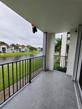 Balcony view overlooking a grassy area and a water body, with multiple residential buildings in the background.