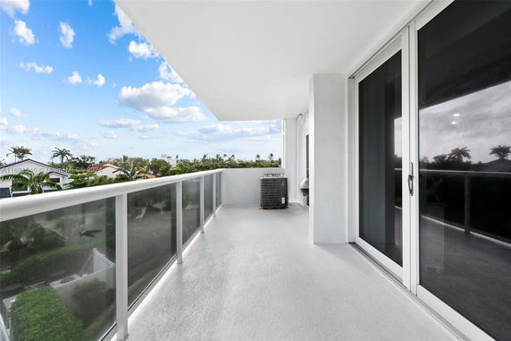 Balcony view with glass railing and a view of rooftops and trees.