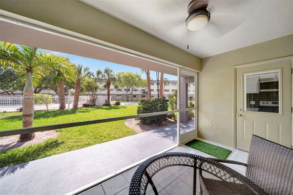 View from a patio showing a grassy area with palm trees and a building in the background.
