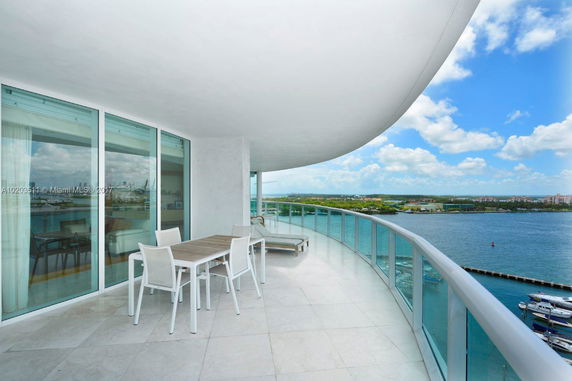 Curved balcony with glass railing overlooking water and distant buildings.