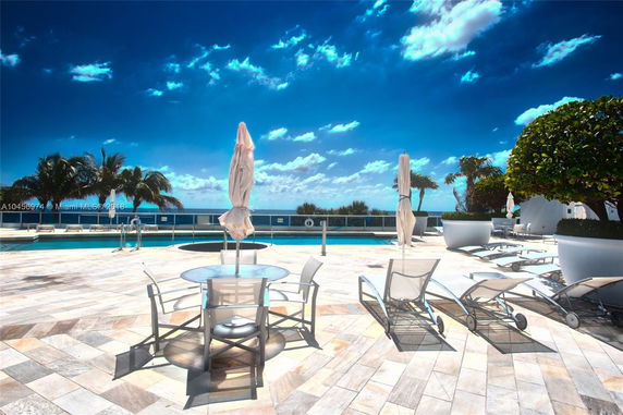 Outdoor swimming pool area with lounge chairs and umbrellas on a paved deck.