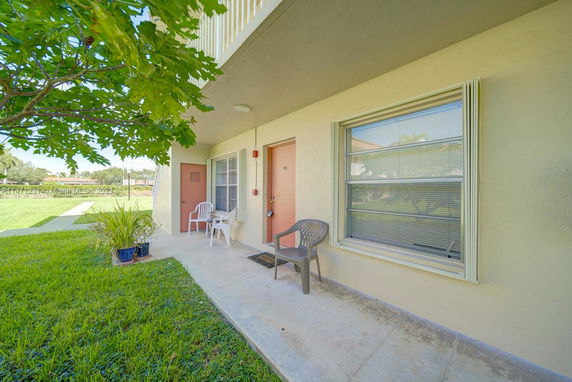 Front view of a small apartment unit with chairs on the porch and a grass lawn.