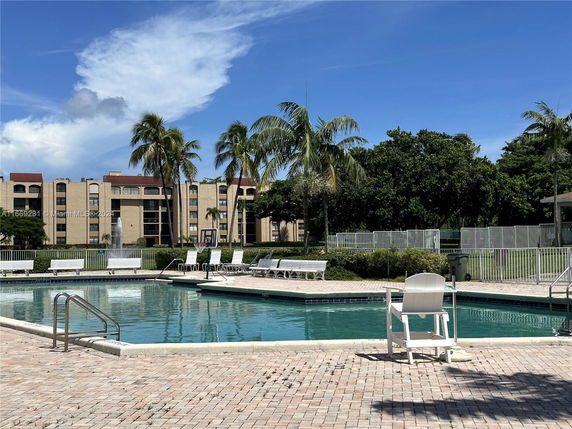 View of a multi-story building with a pool in the foreground and palm trees nearby.