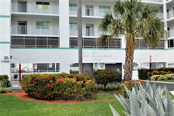 Front view of a multi-story building with balconies and a palm tree in front.