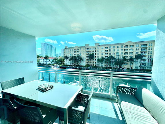 Balcony view with a table and chairs overlooking a waterfront and nearby buildings.