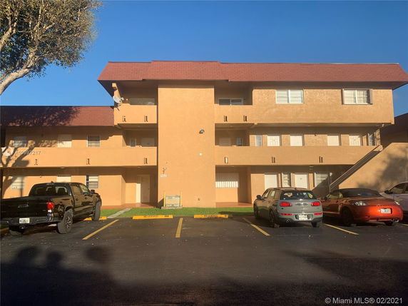 Front view of a multi-story building with several balconies and parking spaces in front.