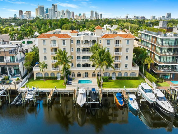 Front view of a multi-story building with balconies and waterfront access, showcasing a pool and nearby boats.