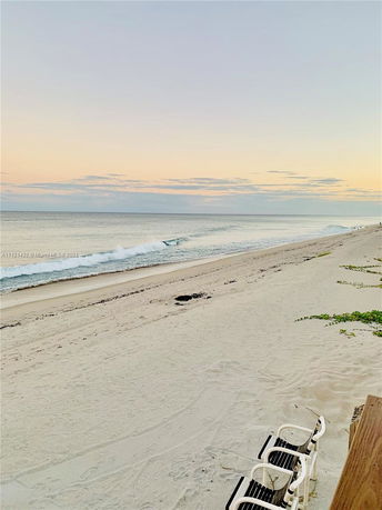 Wide view of a sandy beach with waves and a sunset sky.