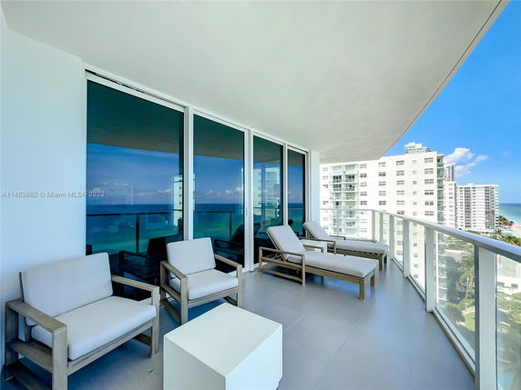View from a balcony with seating area overlooking buildings and ocean.