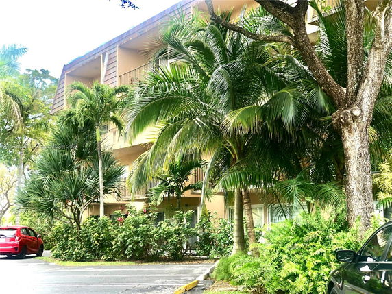 Front view of a multi-story building with balconies surrounded by lush greenery.