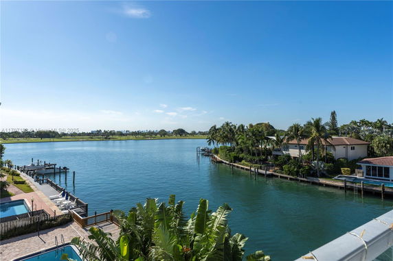 Wide view of a waterfront with houses and palm trees along the shoreline.