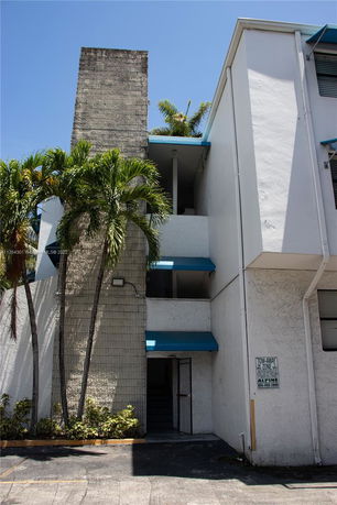 Front view of a building with a blue awning and palm trees.