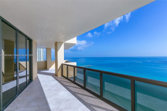 Panoramic view from a balcony overlooking the ocean, with glass railings and tiled flooring.