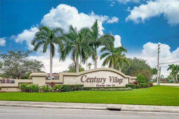 Front view of a community entrance with palm trees and signage.