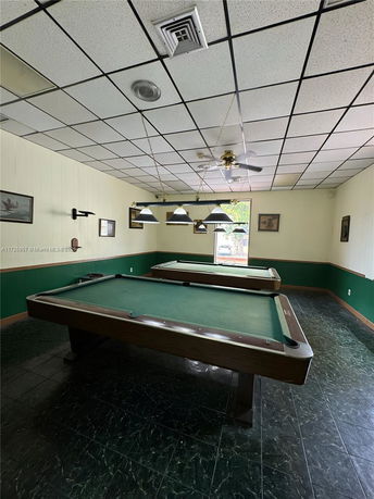 Room with two billiard tables and ceiling lamps.