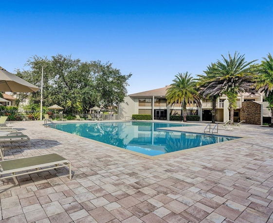Outdoor swimming pool area with surrounding lounge chairs and palm trees.