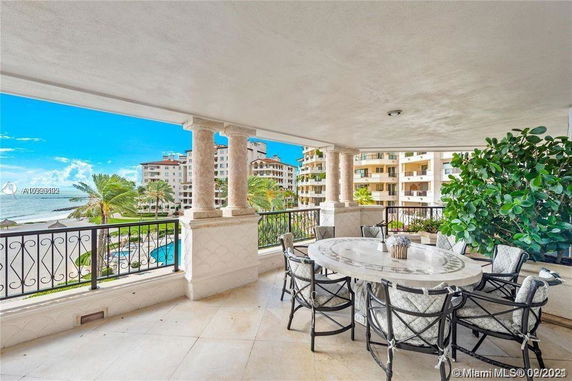 Balcony view from a luxurious building overlooking a landscaped area with a pool, palm trees, and adjacent apartment buildings.