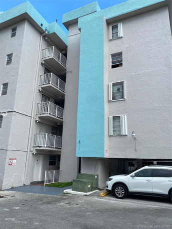 Front view of a multi-story building with balconies and a parking area.