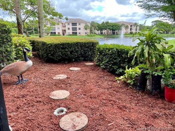 Outdoors area with stepping stones, artificial duck, plants, and view of buildings across a pond.