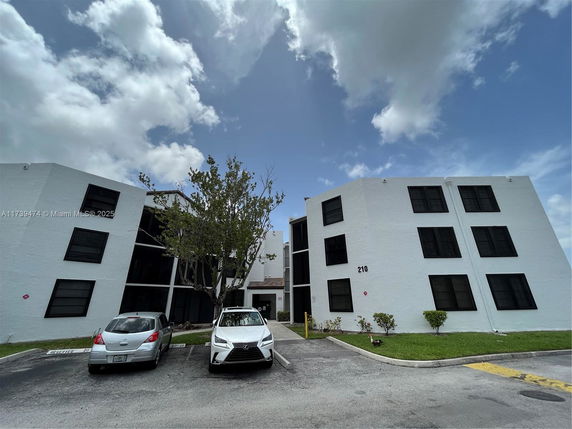 Front view of a multi-story building with several windows and a parking area in front.