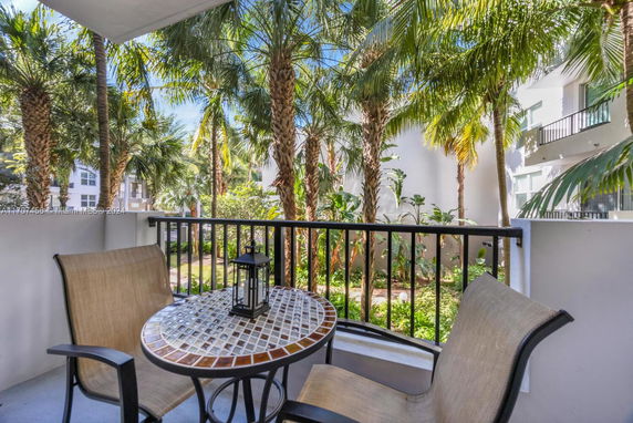 Balcony view of outdoor greenery with palm trees and nearby building.