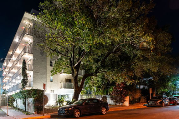 Night view of a multi-story building with illuminated balconies and a large tree in the foreground.
