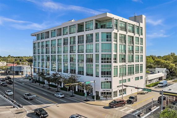 Front view of a modern multi-story building with large windows on a busy street corner.