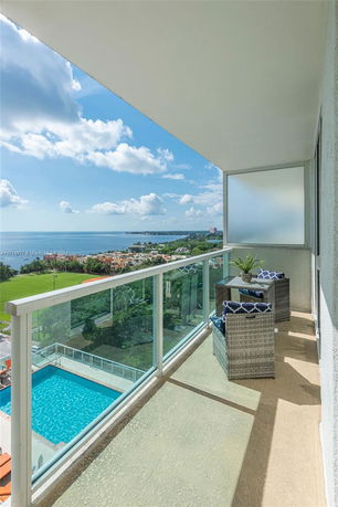 Balcony view from a high-rise building overlooking a swimming pool and a coastal area.