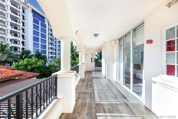 Covered balcony with elegant columns, overlooking nearby buildings and greenery.