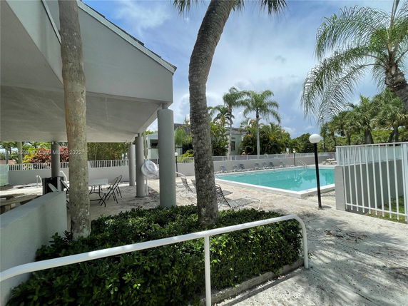 Outdoor swimming pool area with patio seating and palm trees.
