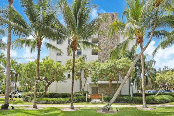 Front view of a multi-story building with a stone facade and surrounded by palm trees.