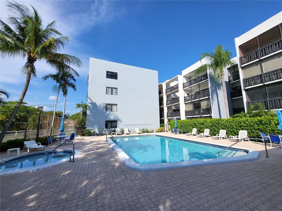 Outdoor swimming pool area with surrounding residential buildings and palm trees.