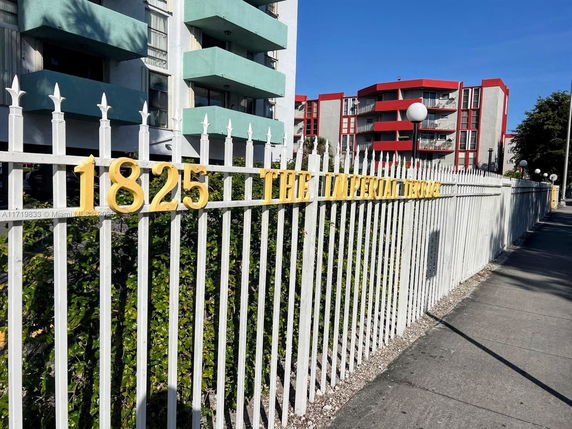 Front view of a multi-story apartment building with balconies and a decorative fence.